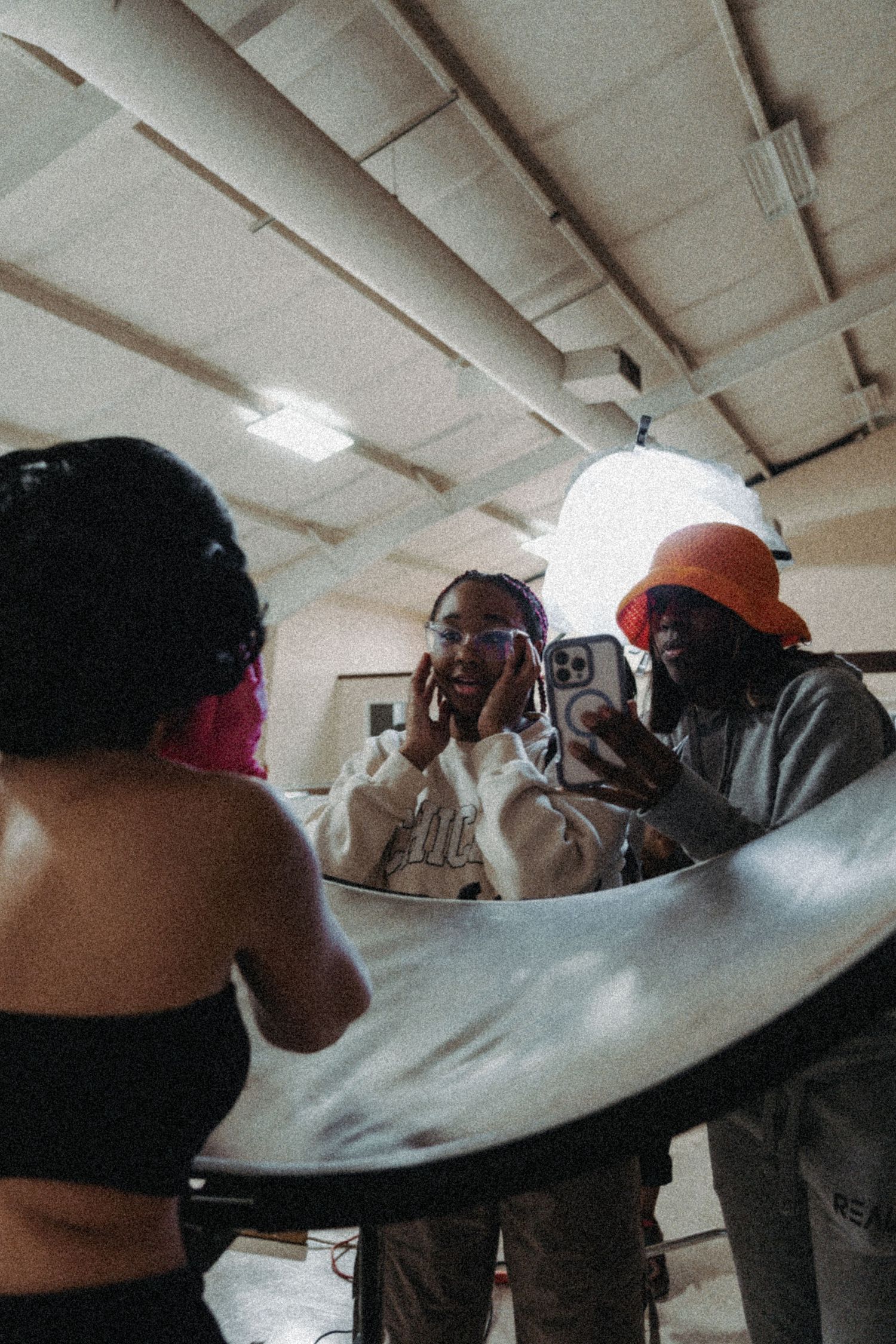 Three people review photos on a smartphone behind a reflector during a studio photo shoot.