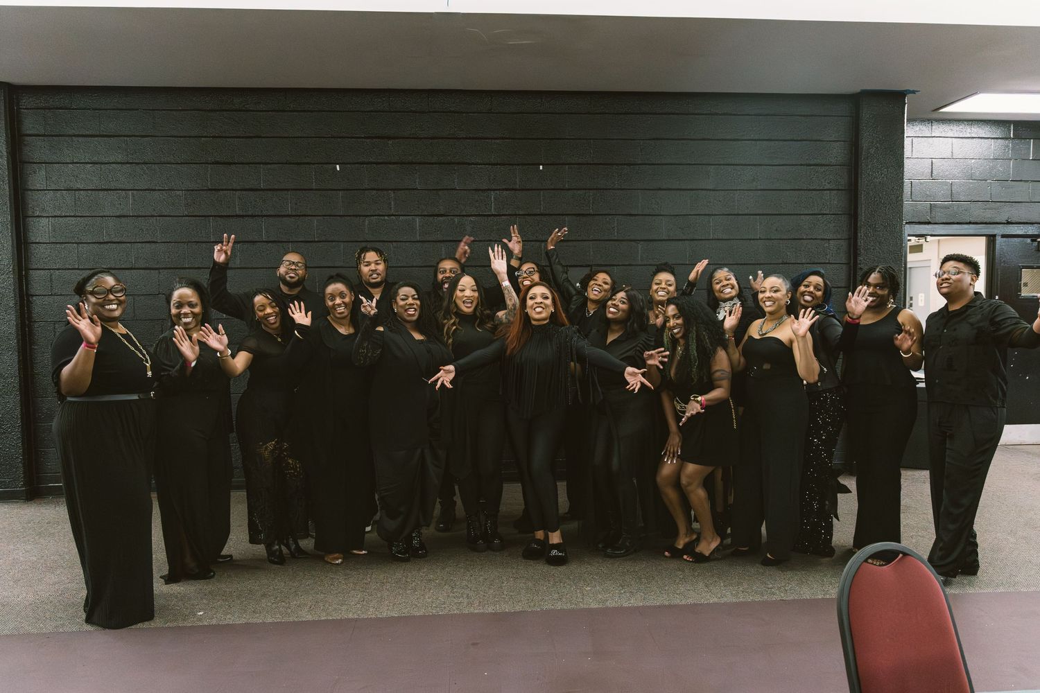Large group of performers in all-black outfits posing together and celebrating after a show.