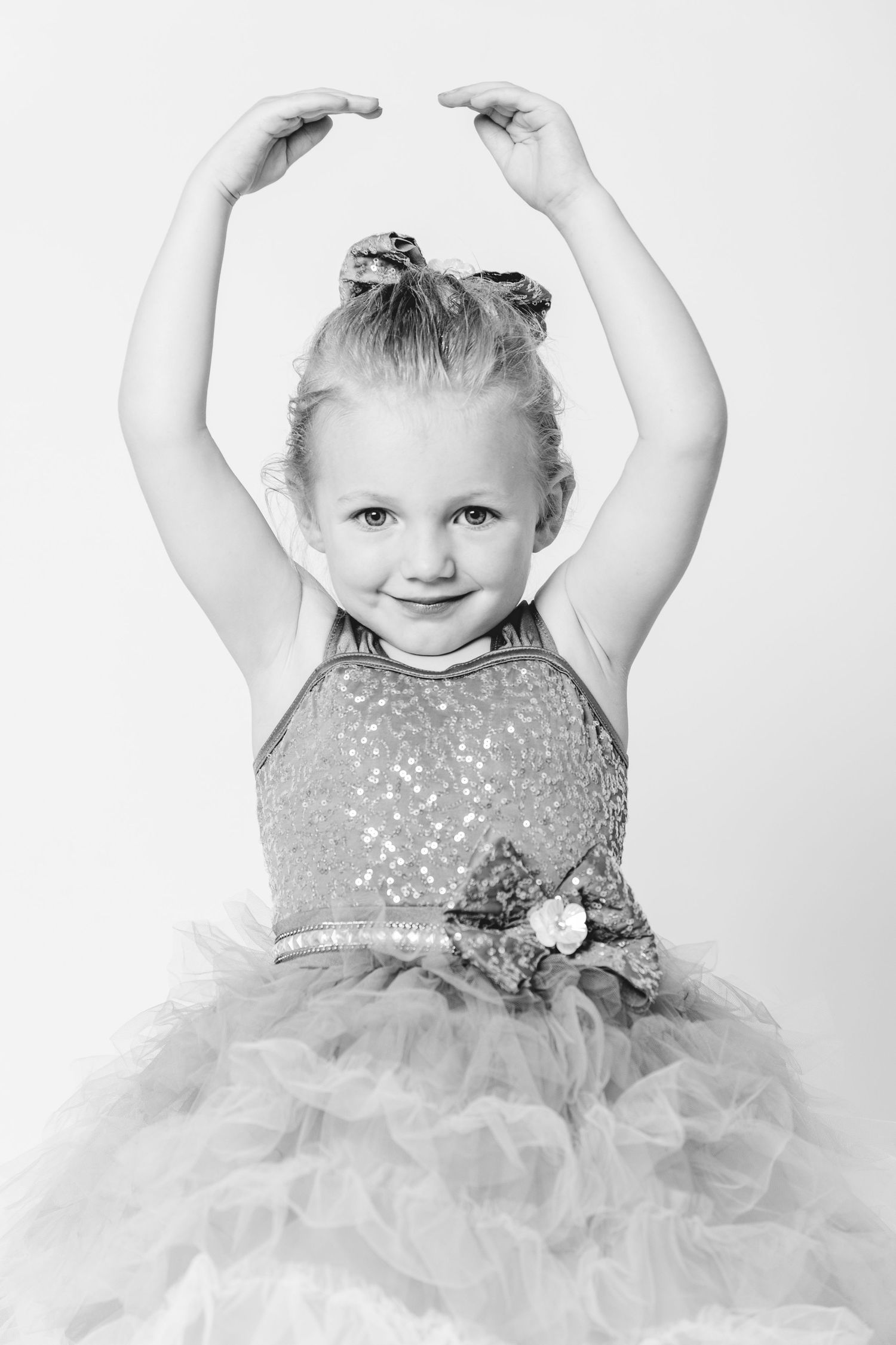 Cute little girl in sequin dress posing with arms raised in black and white.