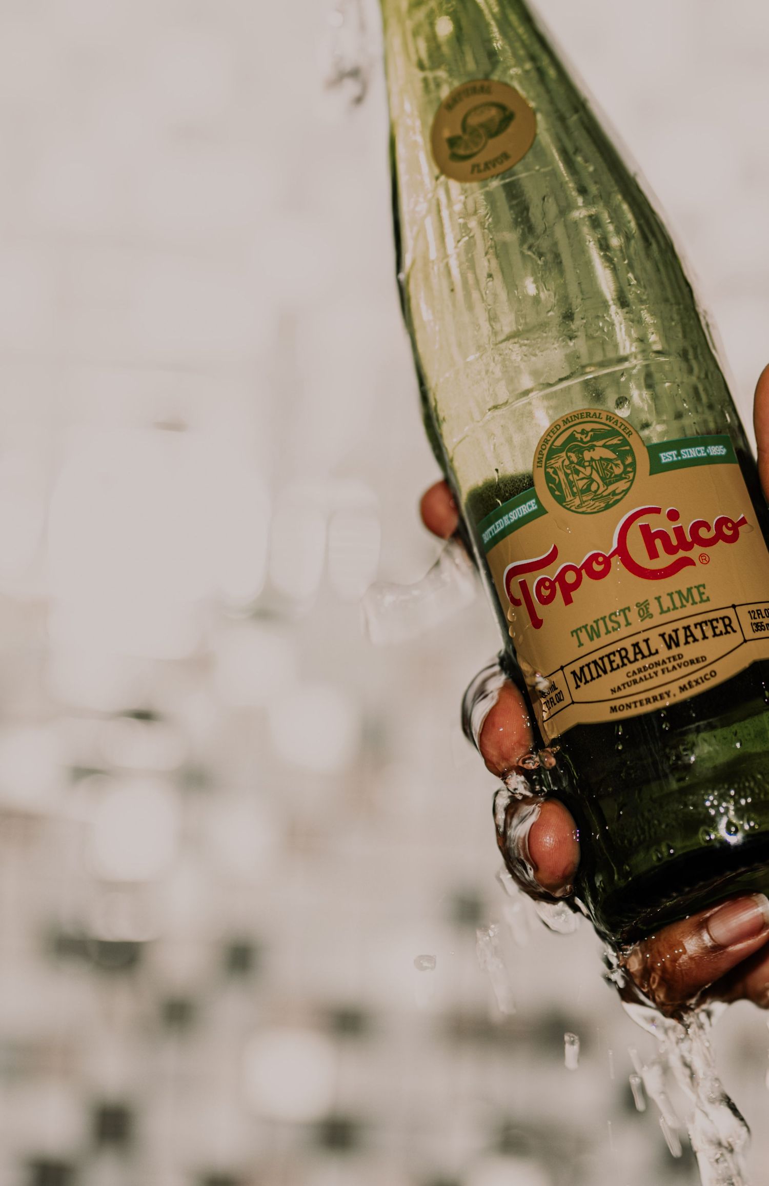 Hand holding a Topo Chico Twist of Lime mineral water bottle with water splashing around.