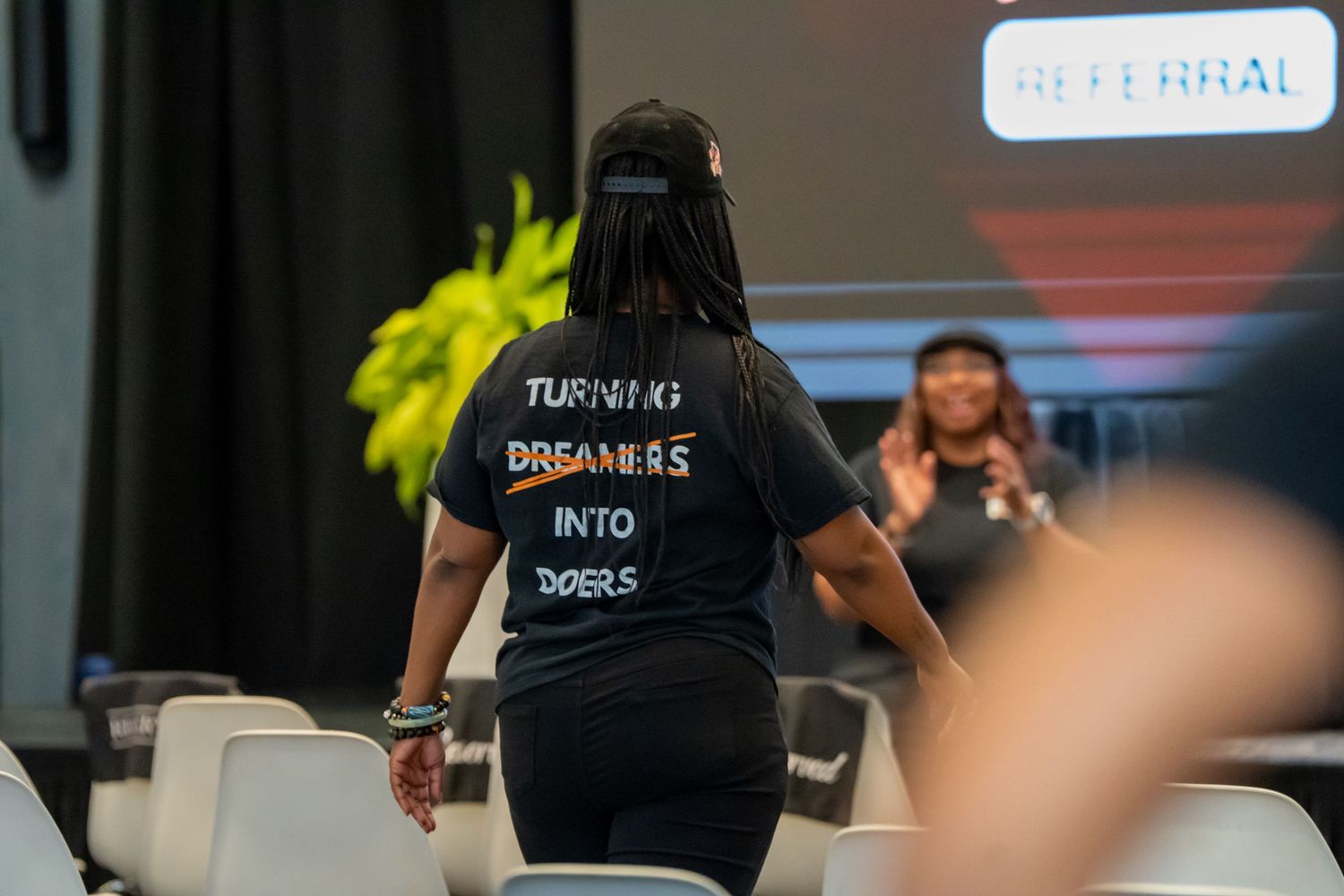 Woman wearing a black t-shirt reading Turning Dreamers Into Doers walking at an event.