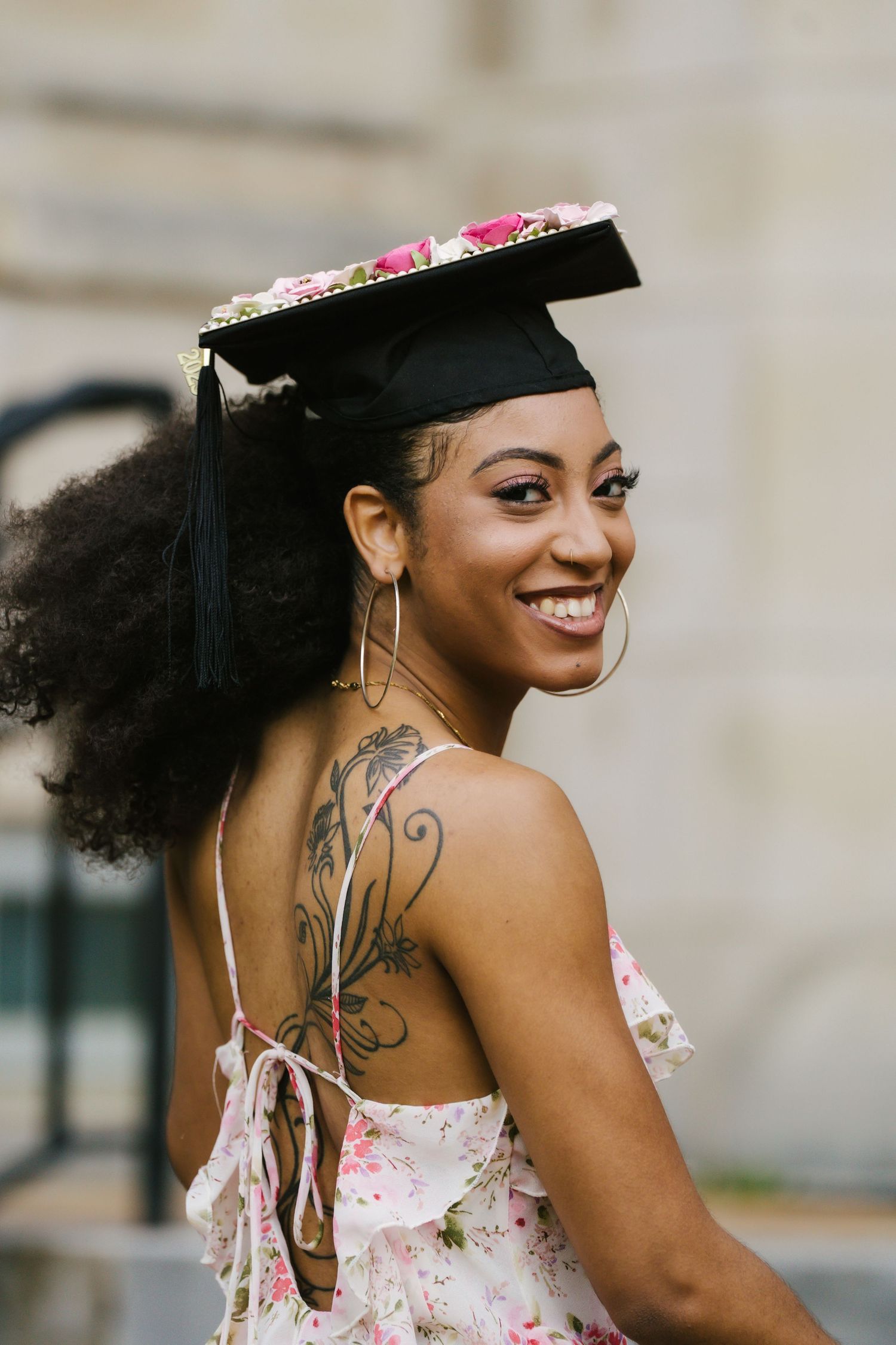 Smiling graduate wearing floral cap and dress with back tattoo visible.