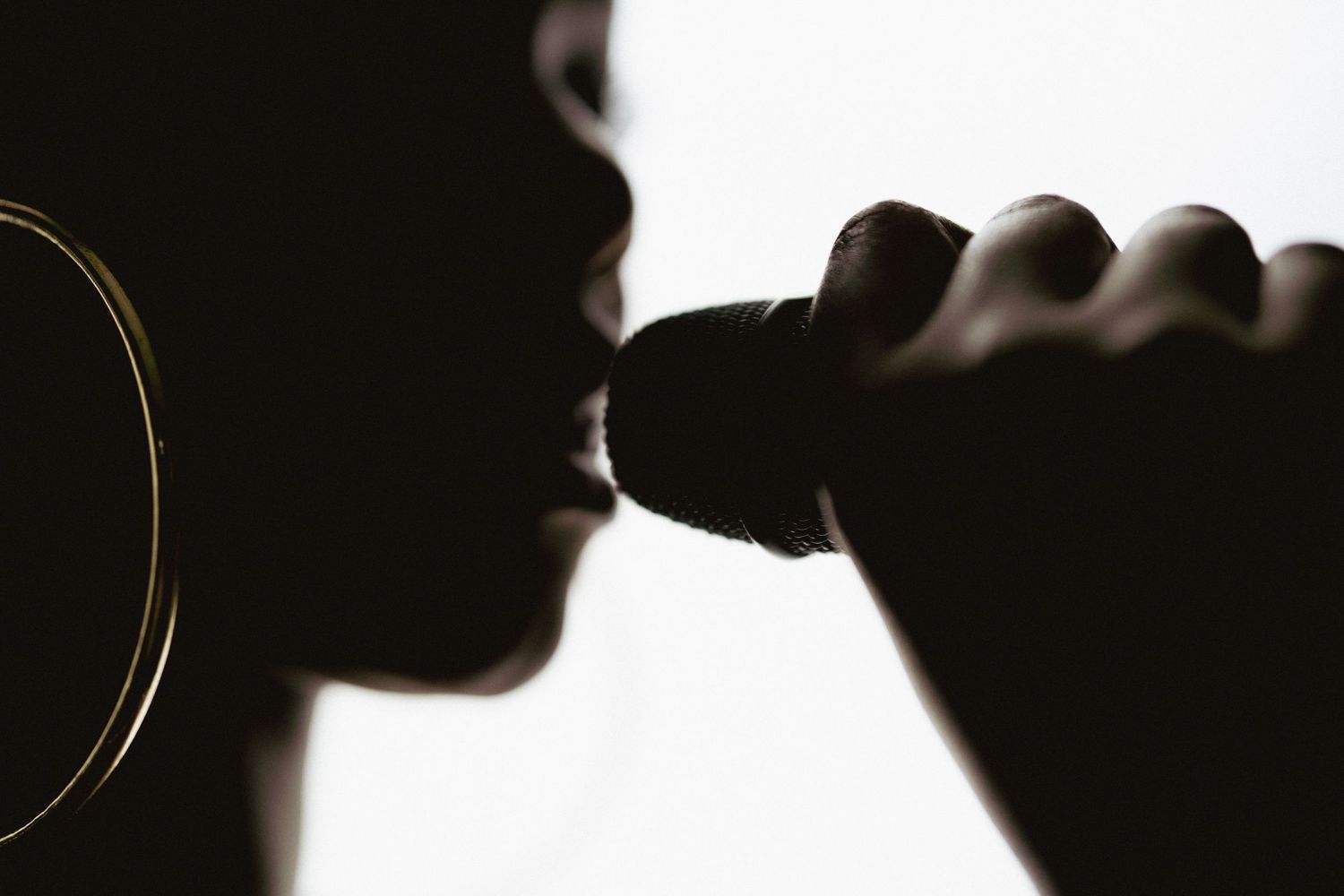 Silhouette profile of female singer holding microphone close to lips with hoop earring visible.