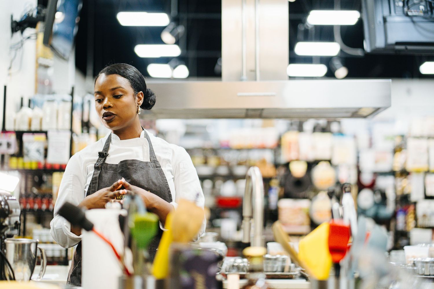 Female chef in black apron prepares ingredients at a professional kitchen station.