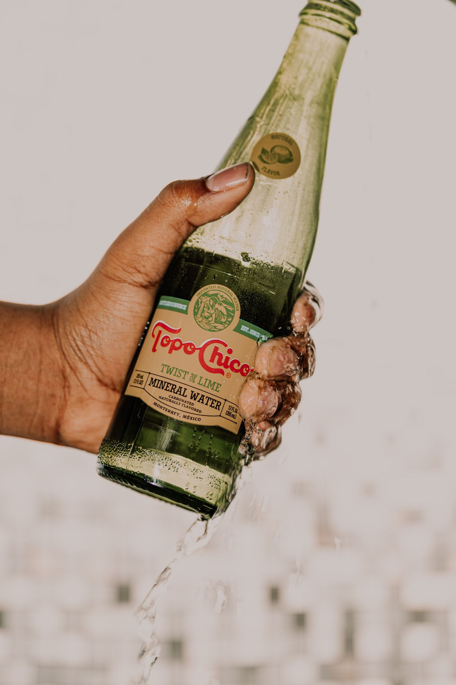 Hand holding a wet Topo Chico Twist of Lime mineral water bottle with water dripping.