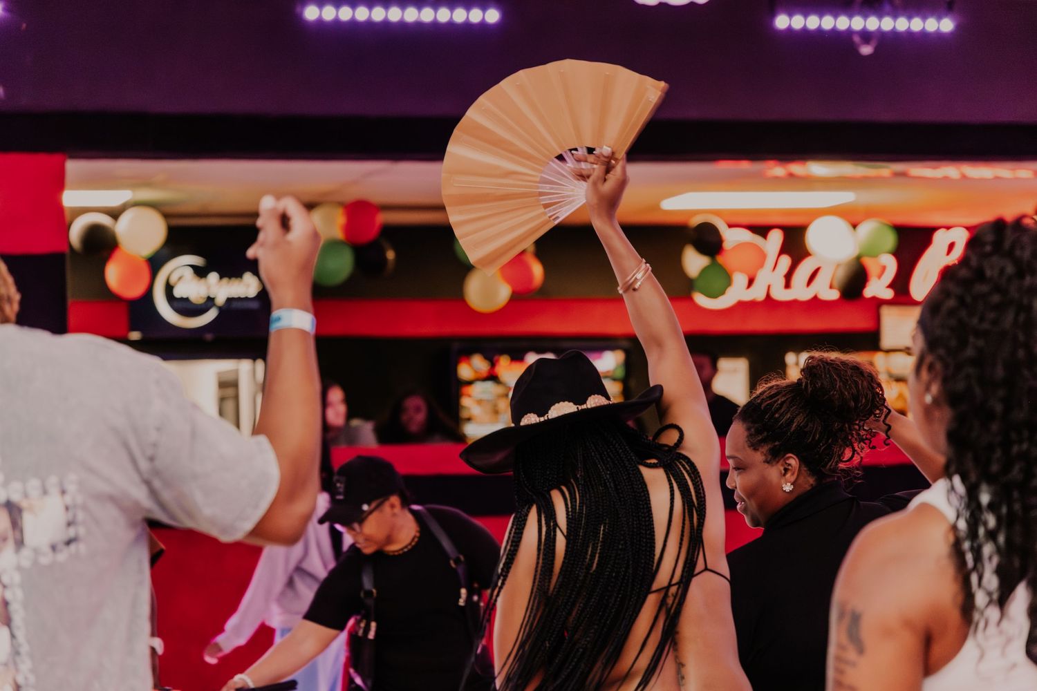 A woman raises a decorative fan while dancing with others at an energetic indoor party.
