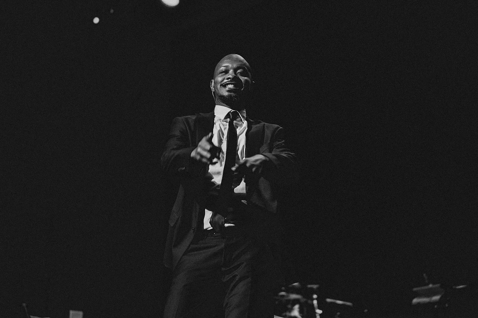 Black and white photo of a man in a suit performing on stage under dramatic lighting.