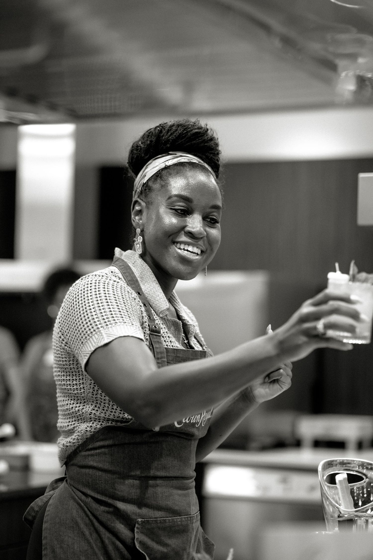 Smiling woman in apron holds a glass in a professional kitchen.