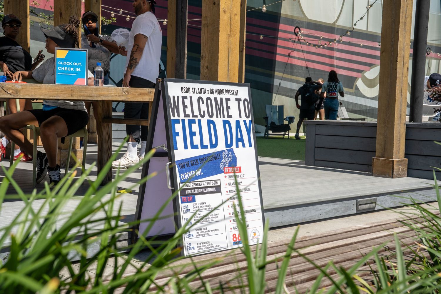 Welcome to Field Day event sign displayed outdoors at a sunny venue with people gathered in the background.
