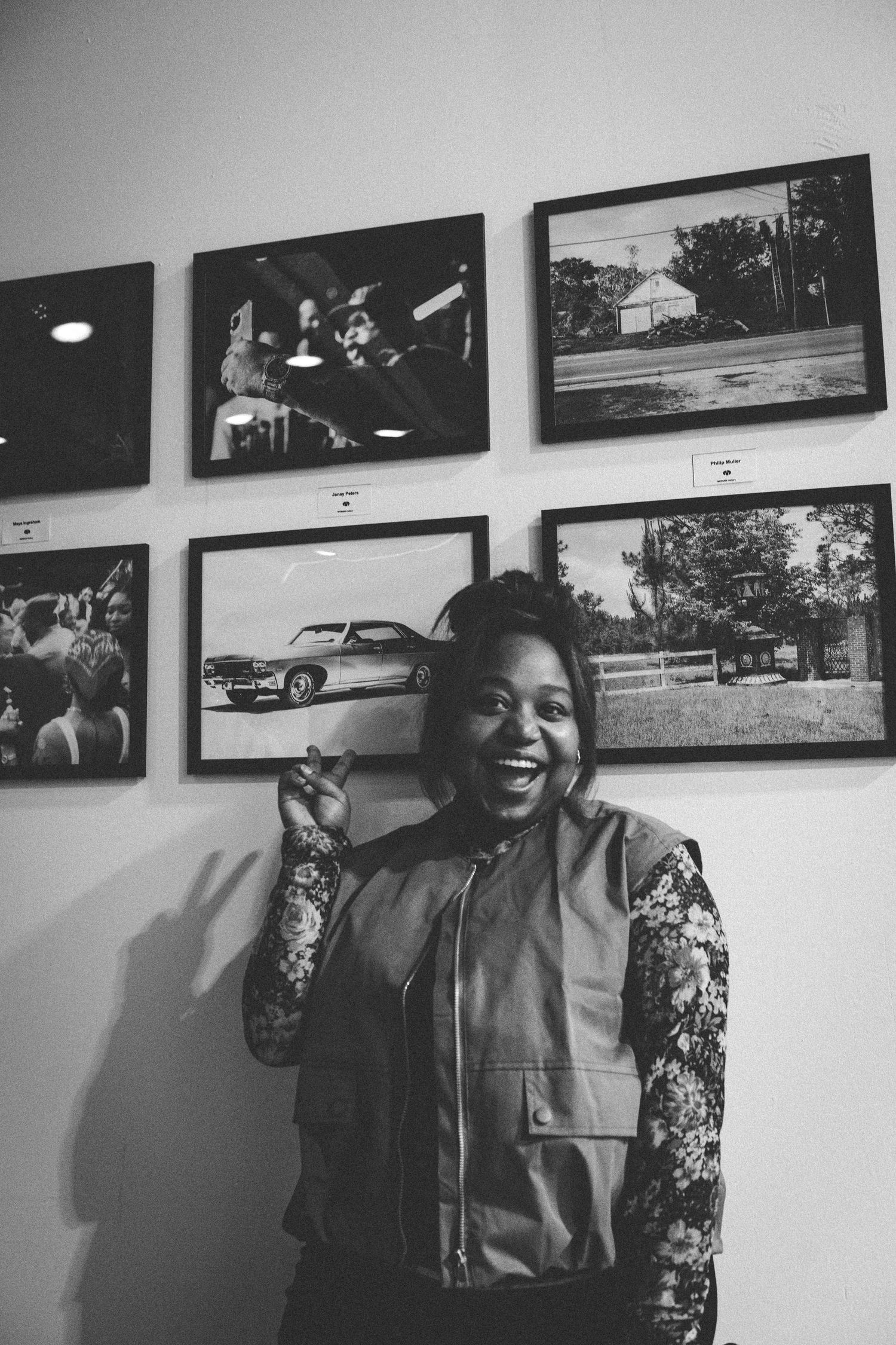 Laughing woman poses in front of framed black and white photography prints displayed on a gallery wall.