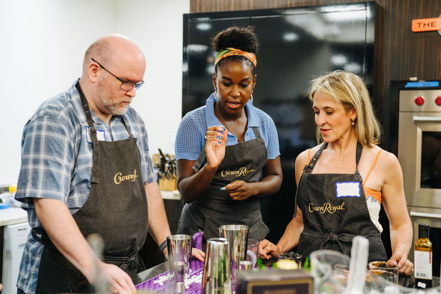Three people in Crown Royal aprons collaborate on a recipe during a cooking class.
