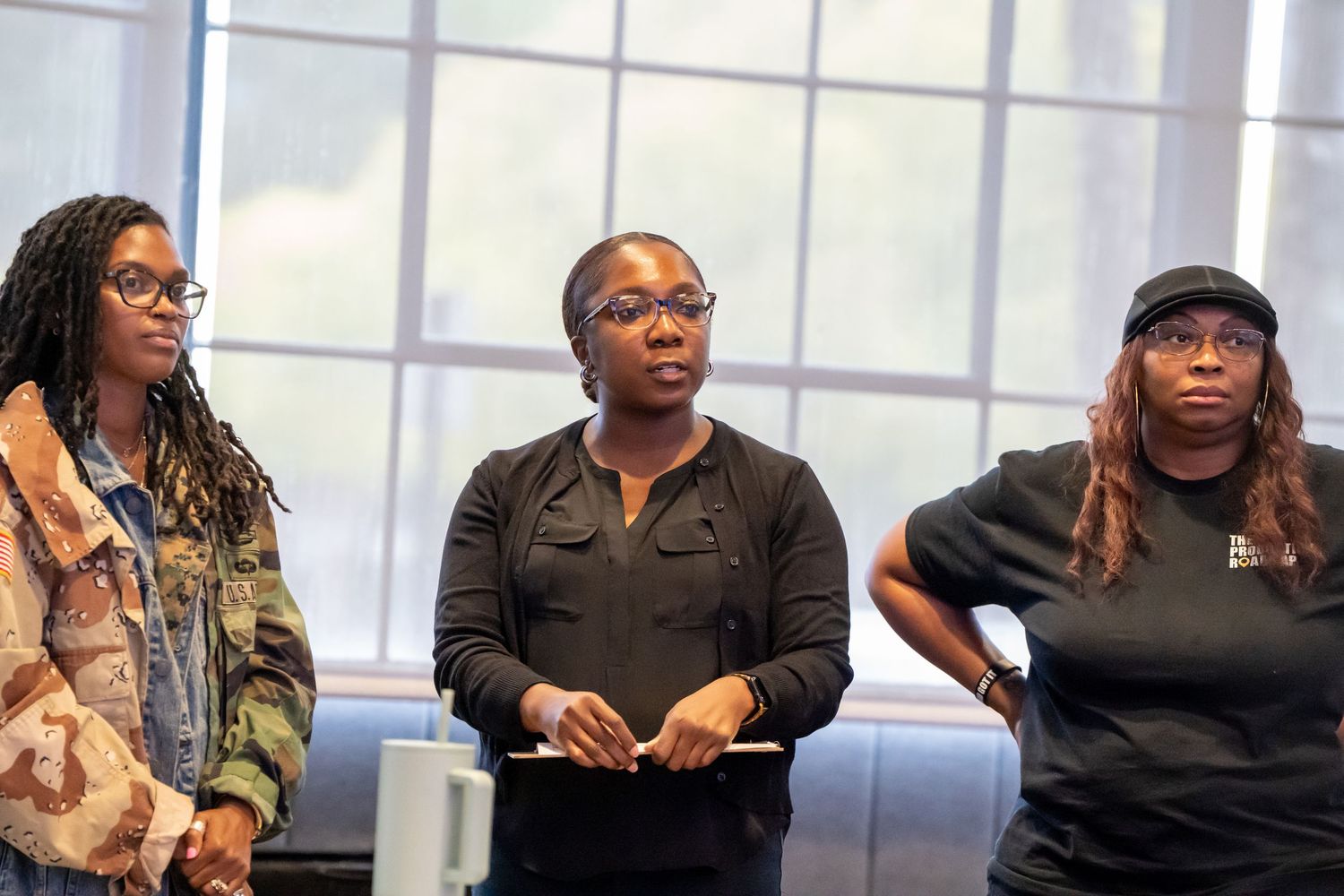 Three women standing together near a window at an indoor workshop or seminar event.