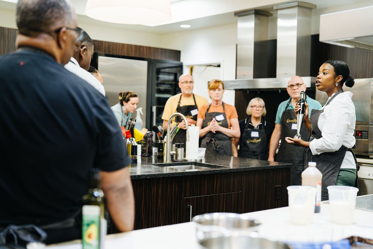 Chef instructs a group of participants wearing aprons during a Crown Royal cooking class.