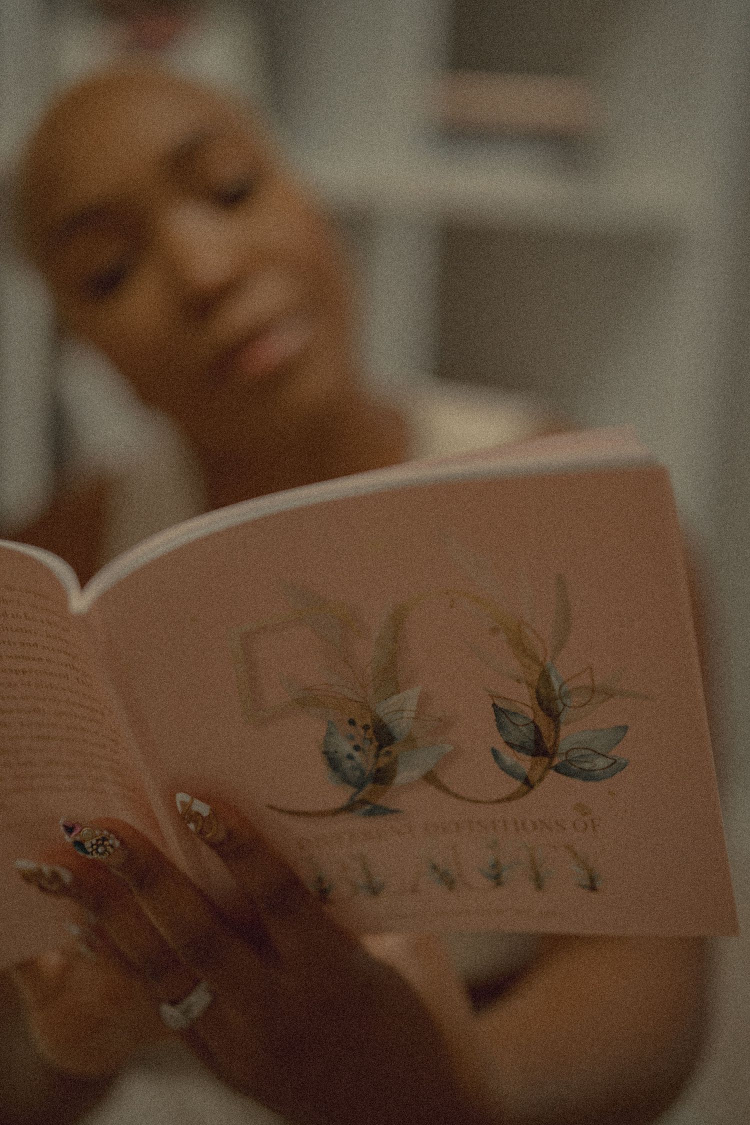 Black woman with short hair reading pink floral book with decorated nails closeup.