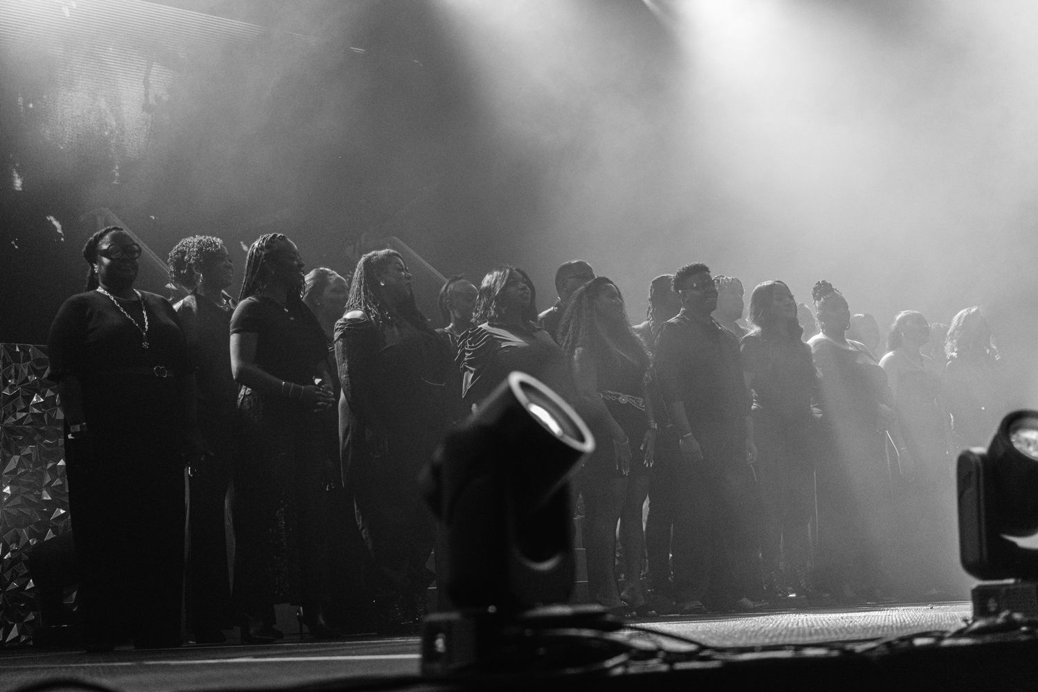 Black and white silhouette of choir or performers standing on a fog-filled concert stage.