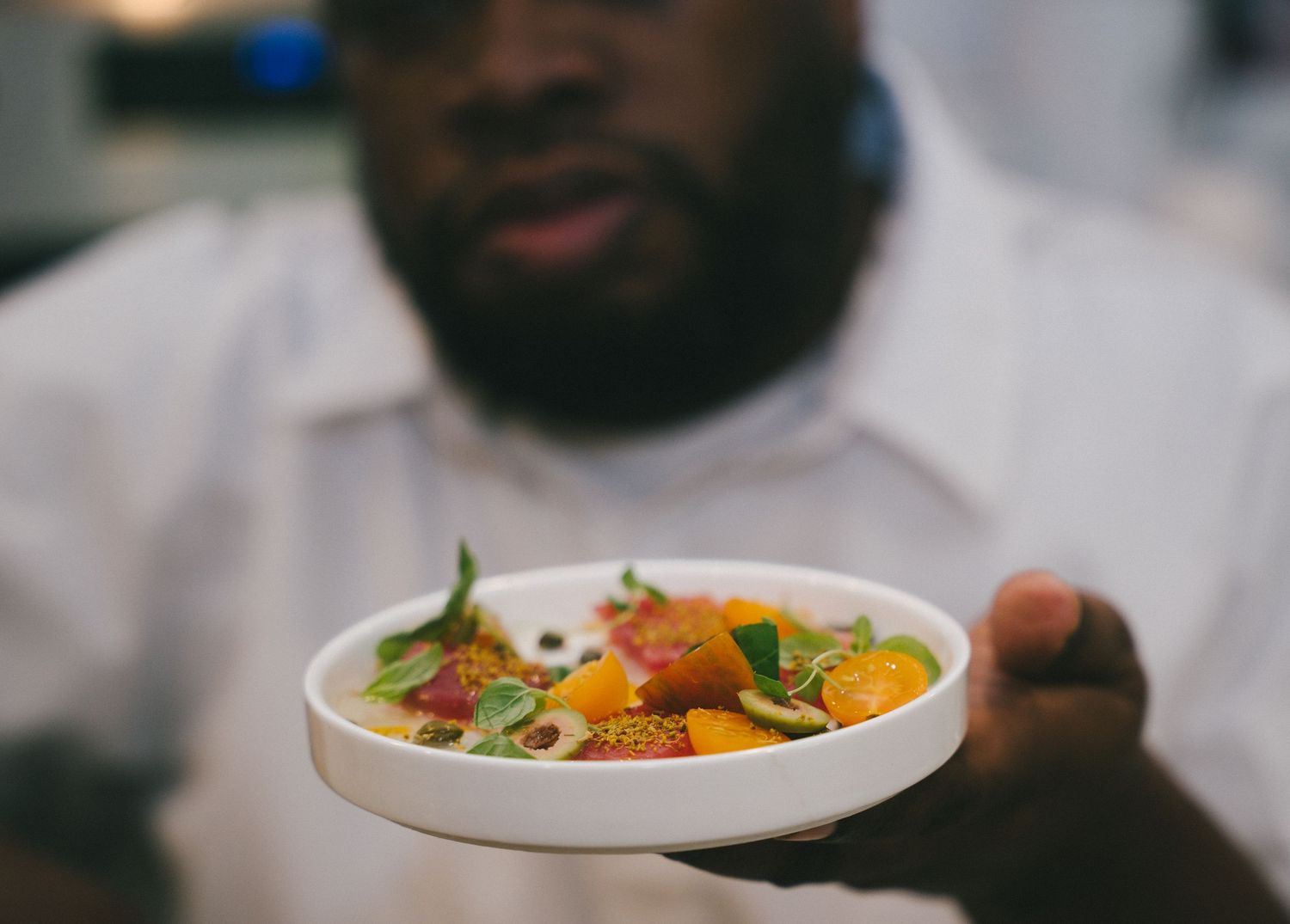 Chef presenting a gourmet colorful salad dish with fresh herbs and vegetables in white bowl.