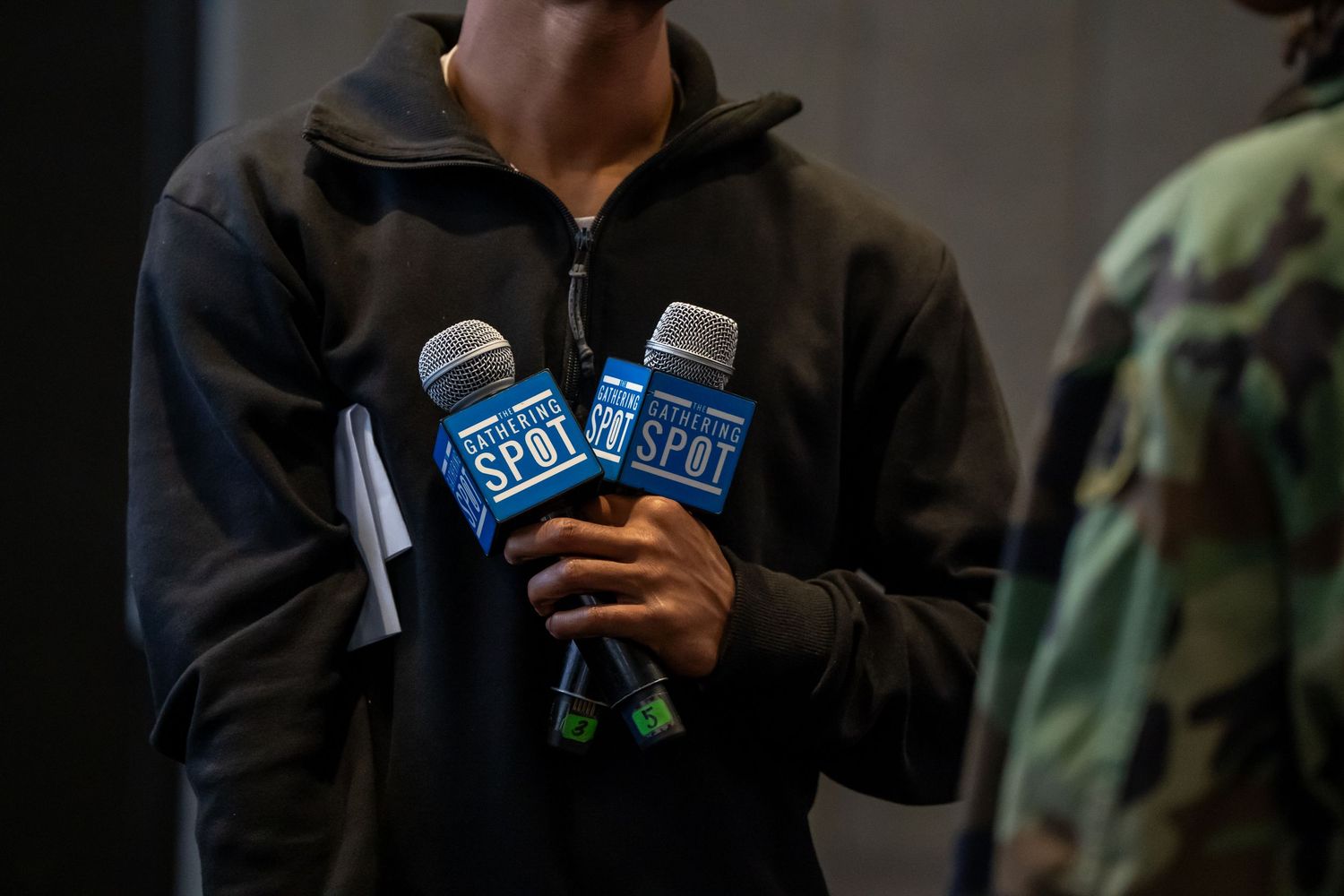 Person holding two microphones with The Spot branding at an indoor event.