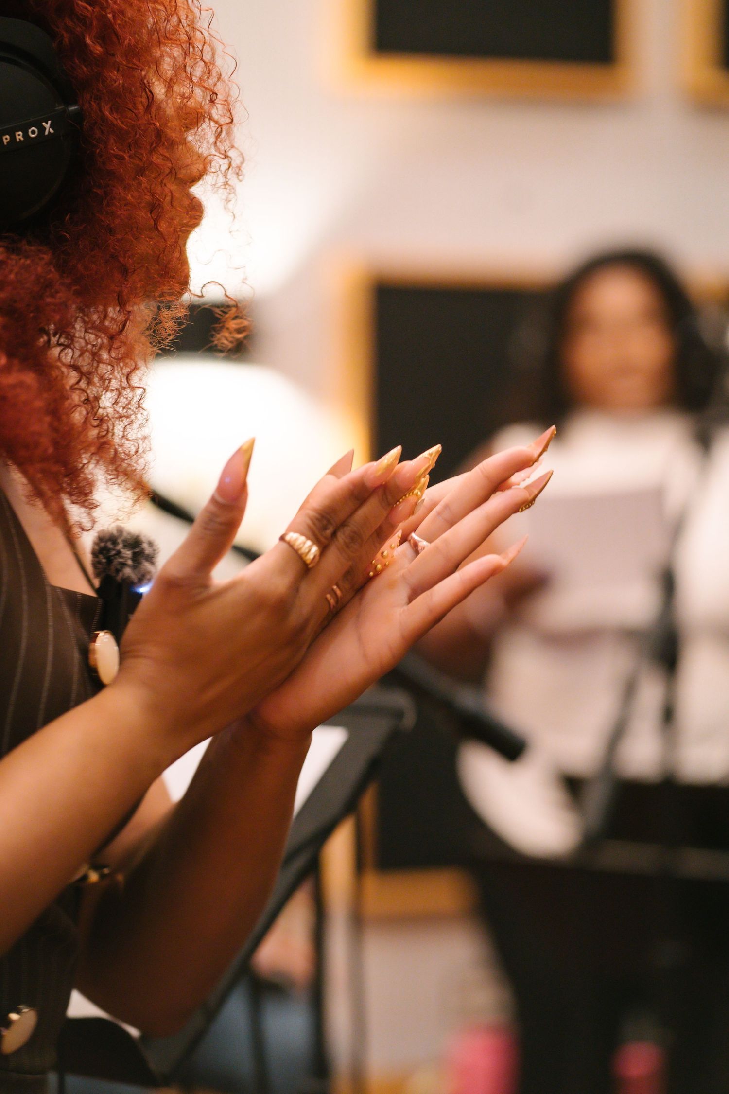 Close-up of woman with red curly hair and gold rings clapping hands in a recording studio.