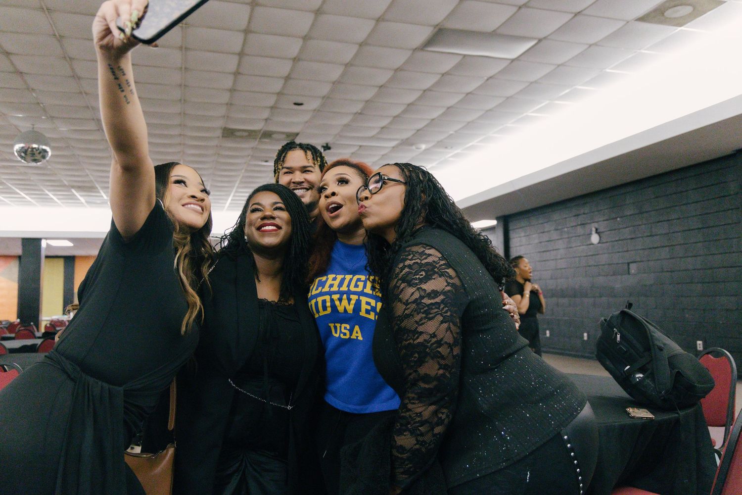 Group of five friends taking a selfie together after a performance in a backstage area.