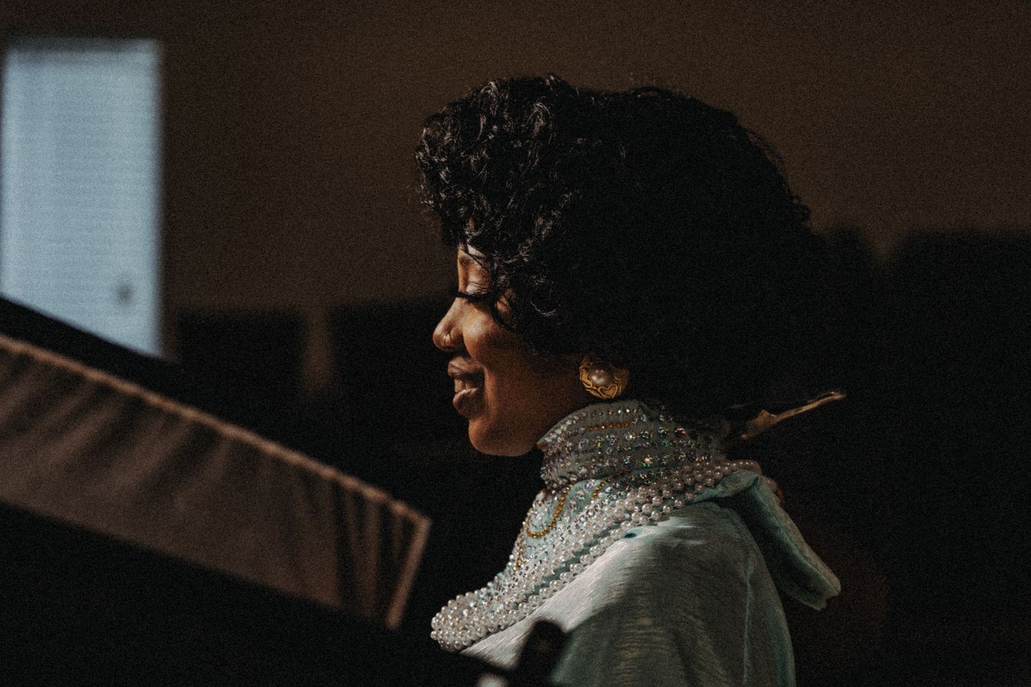 A woman with curly hair and gold earrings performs or speaks at a dimly lit event.