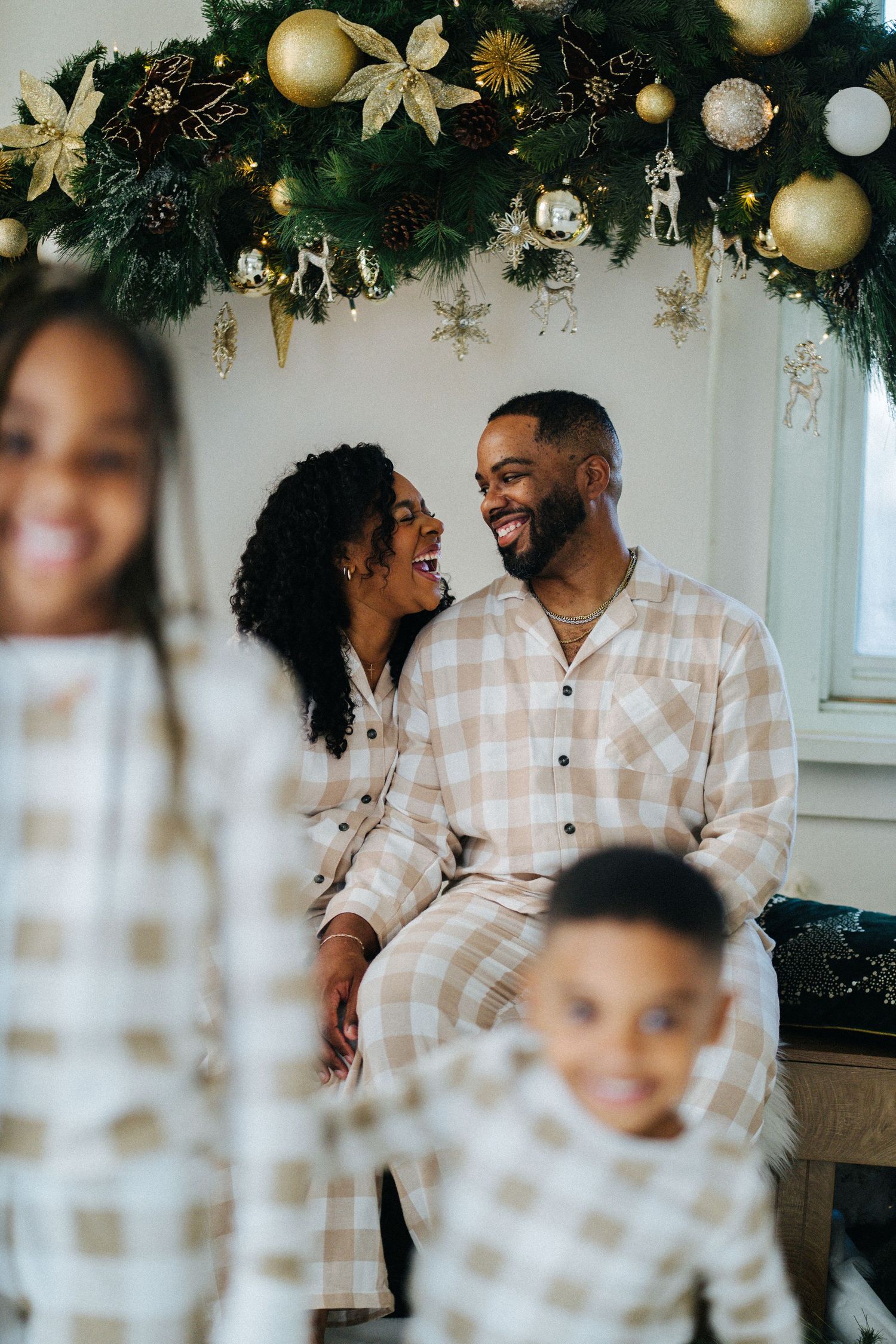 Black couple in matching plaid pajamas smiling at each other under Christmas garland.