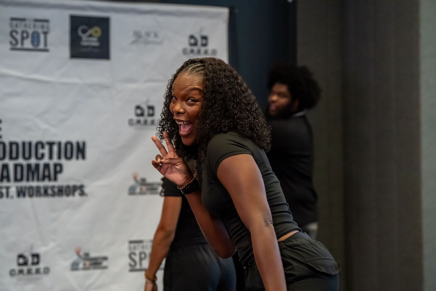 Woman smiling and posing playfully in front of a film production workshop backdrop.