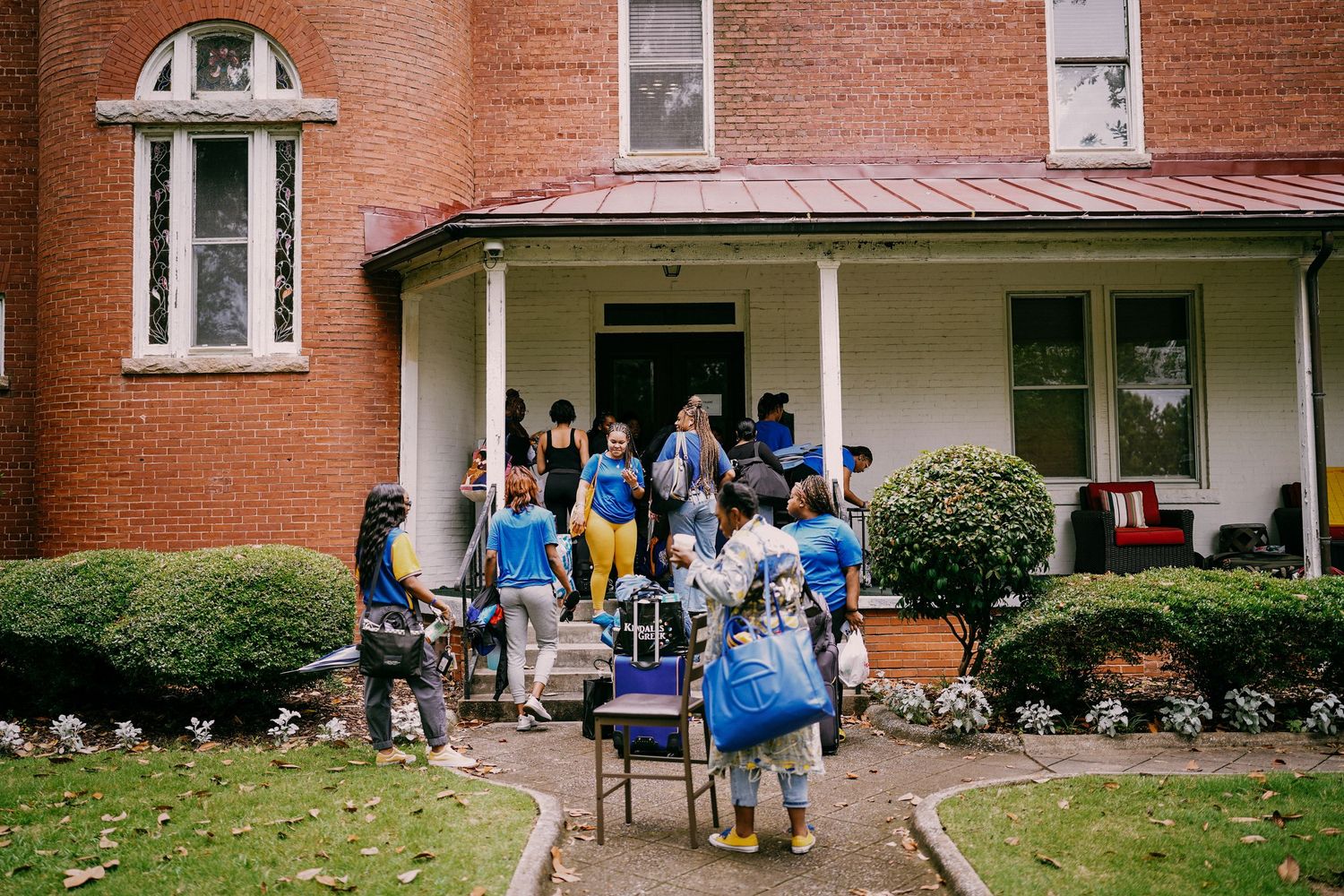 Group of people in blue shirts carrying equipment outside a brick building with a red roof.