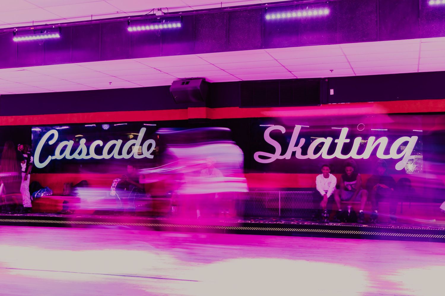 Motion-blurred neon sign reading Cascade Skating glows in vibrant pink and purple lights.