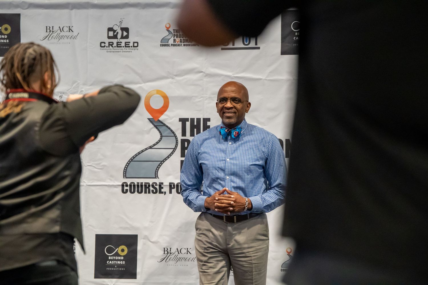 Man in blue shirt smiles at event with Black Hollywood branding backdrop.