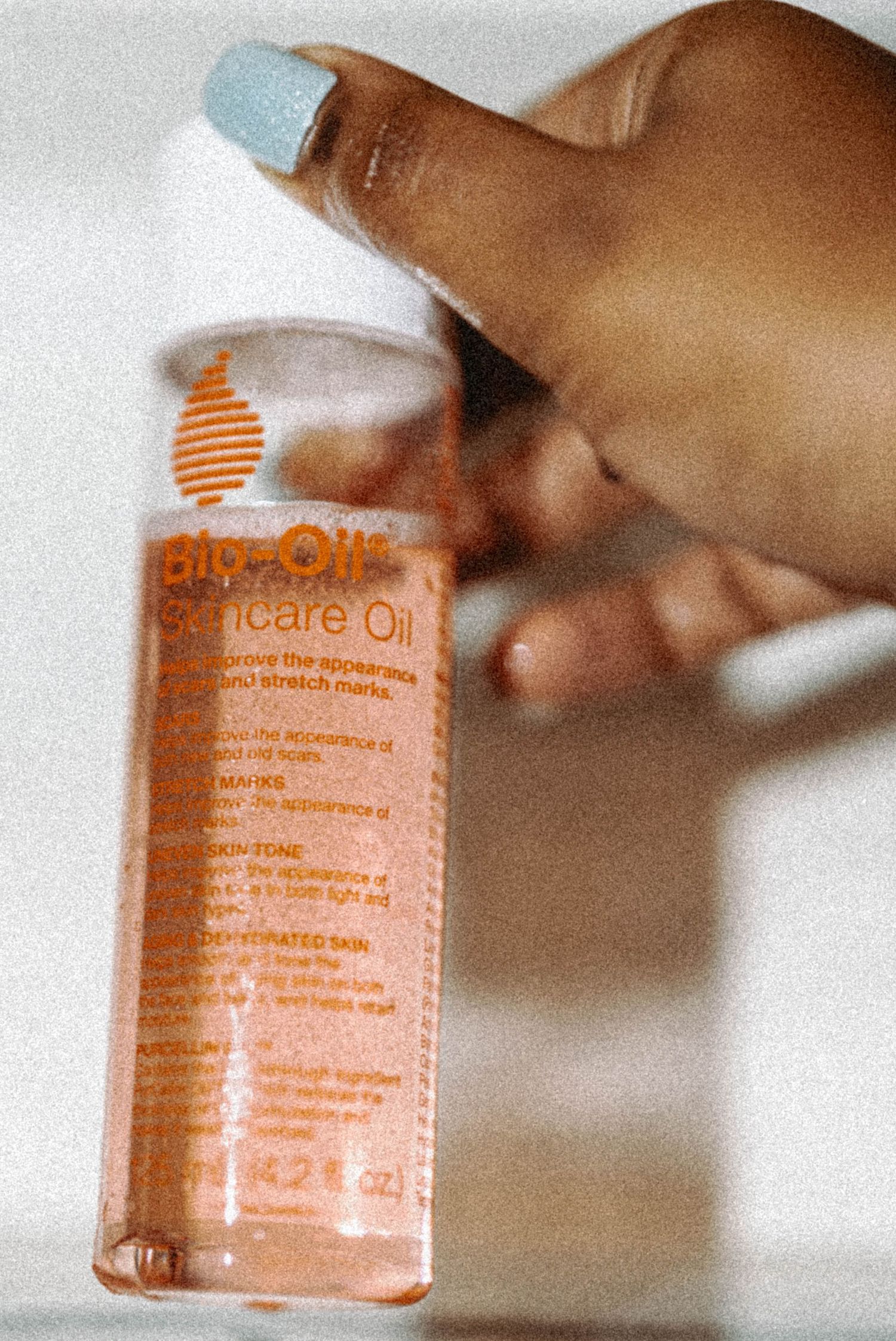 Hand with blue nail polish holding a Bio-Oil Skincare Oil 4.2 oz bottle overhead.