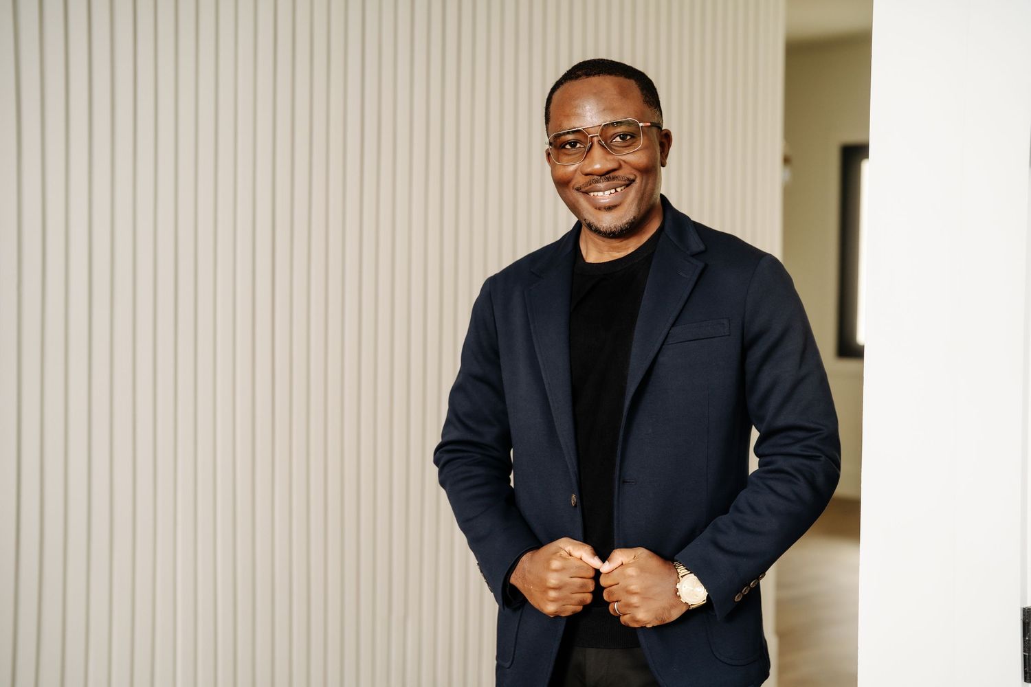 Confident man in navy blazer smiling with hands clasped indoors.