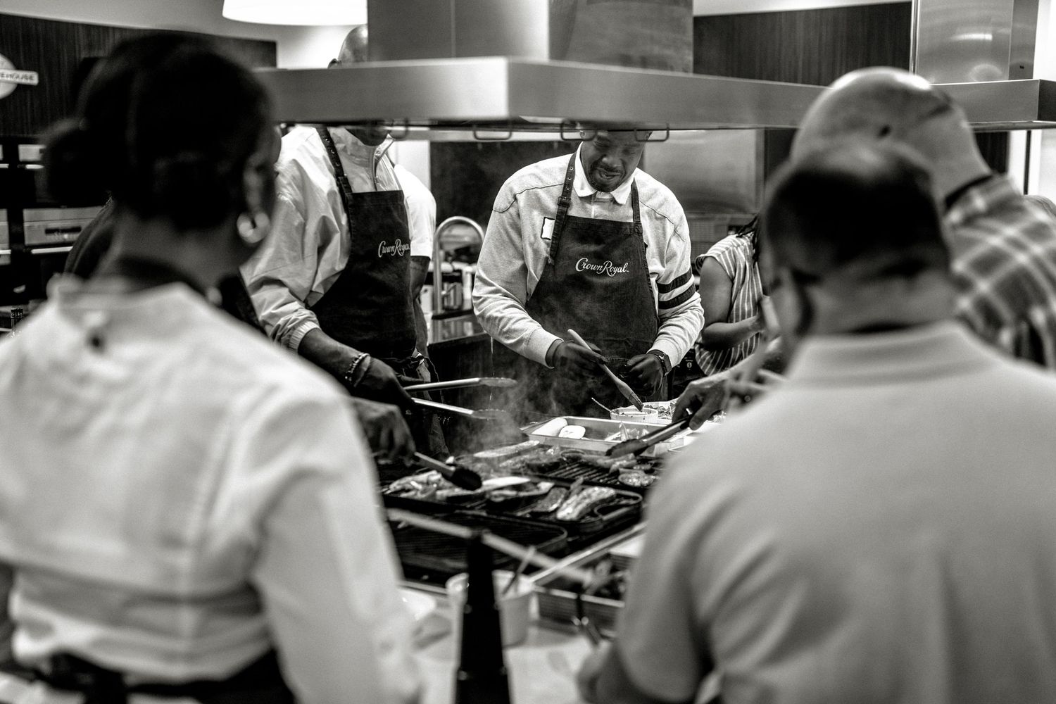 Chef grills food in a busy commercial kitchen with onlookers.