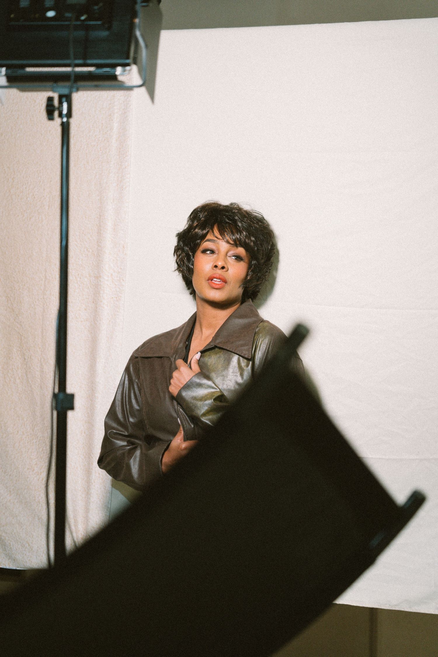 A woman in a brown leather jacket poses confidently in front of studio lighting equipment.