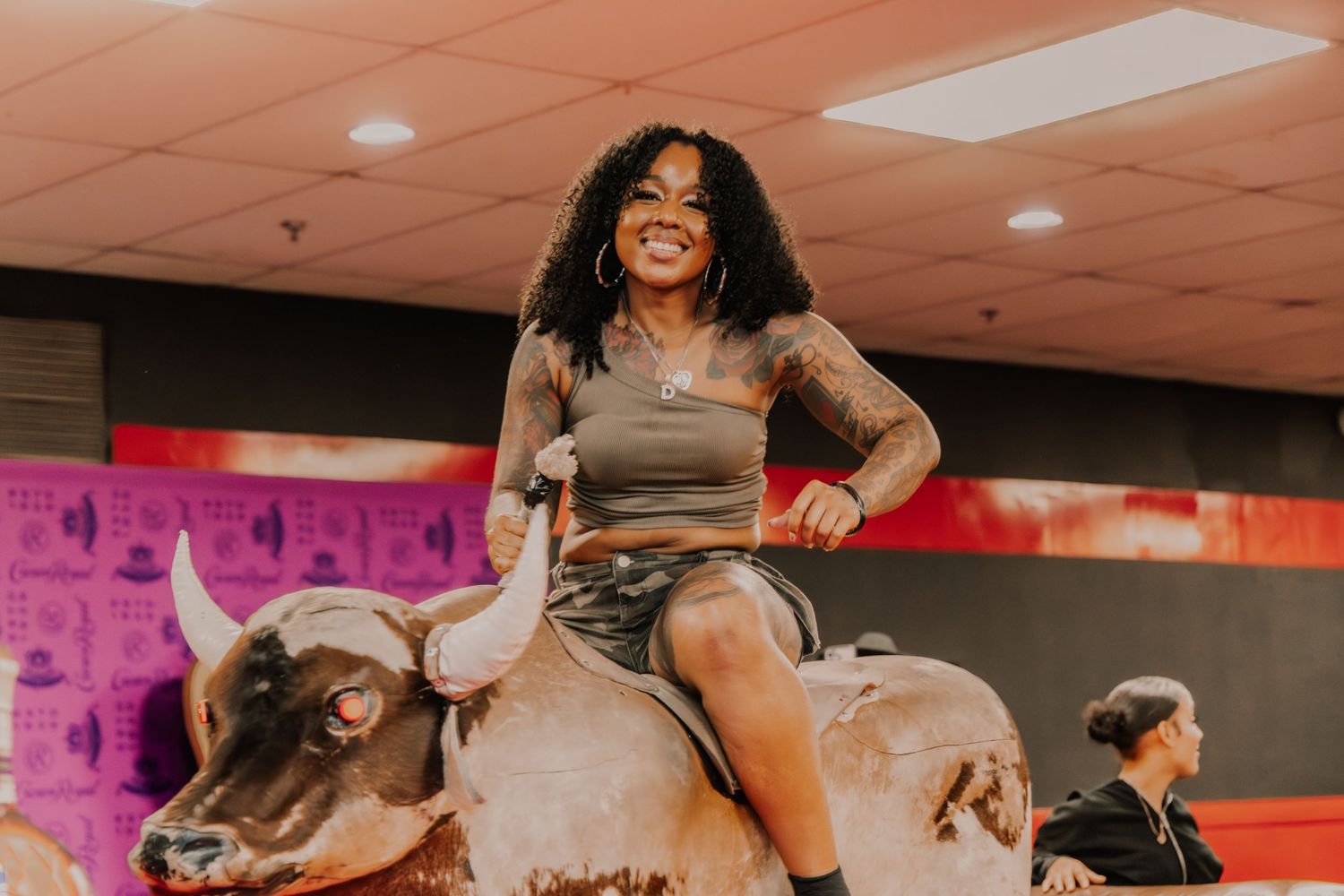 A joyful woman rides a mechanical bull at an indoor entertainment venue during a party.