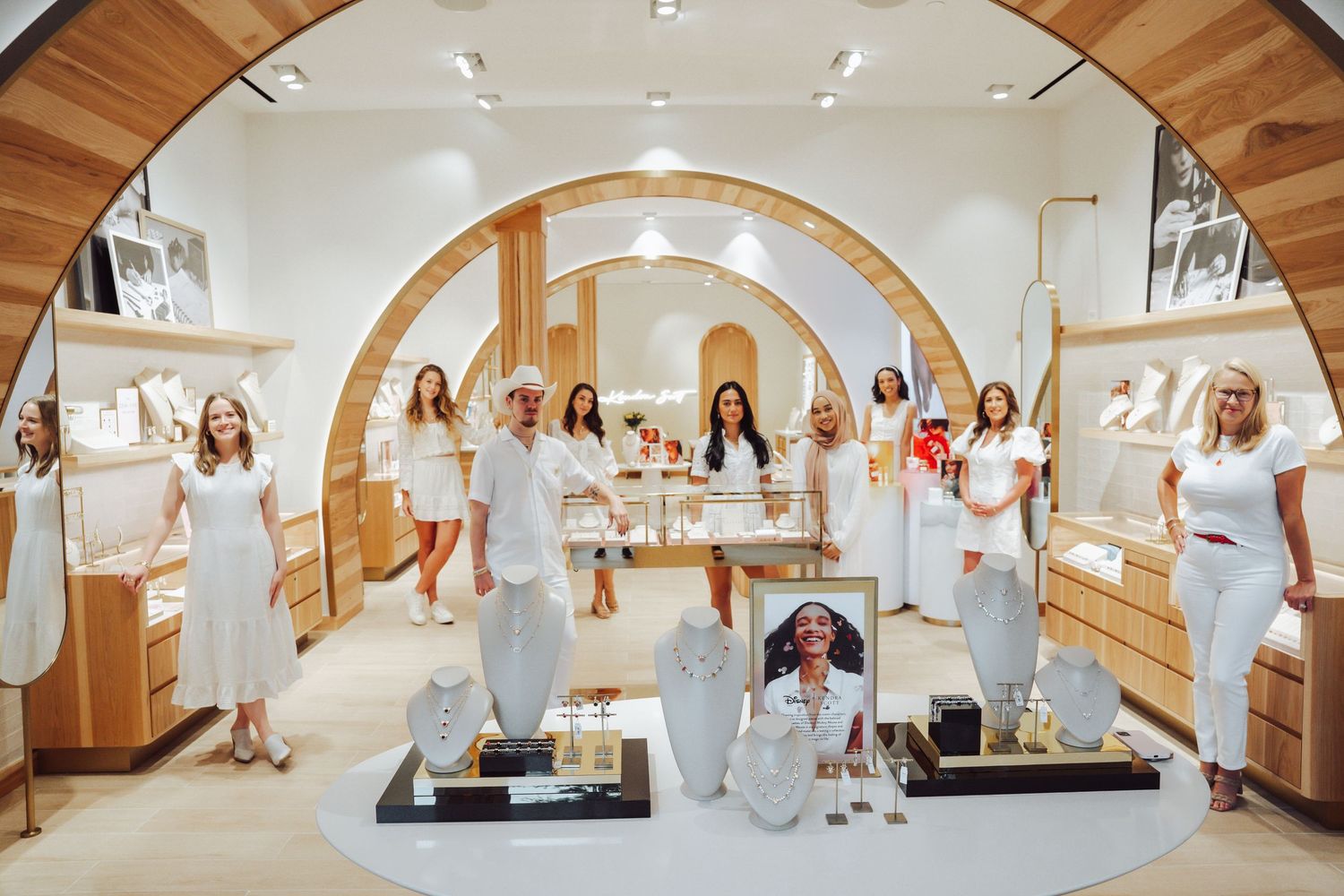 Large group of women in white outfits inside elegant Kendra Scott jewelry store.
