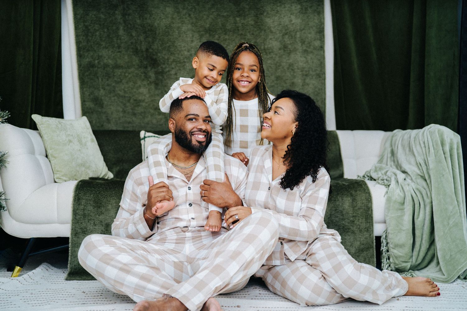 Happy Black family in matching plaid pajamas sitting together on floor smiling.