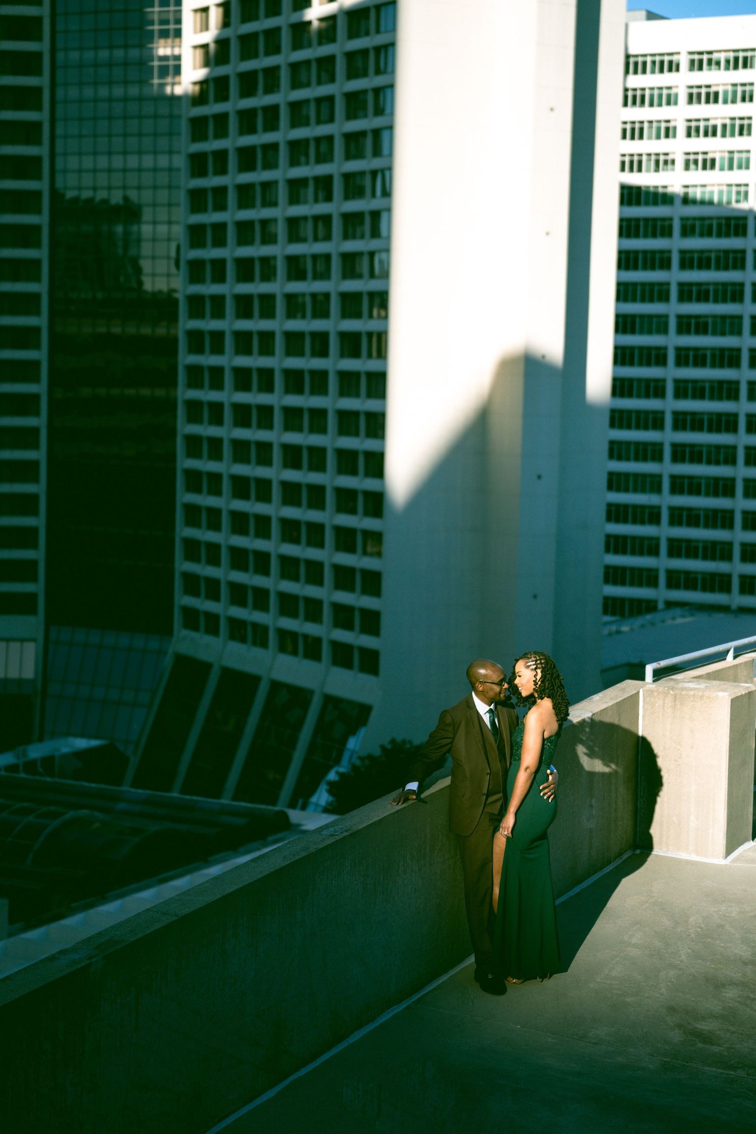 Couple in formal wear sharing romantic moment on rooftop with city skyscrapers backdrop.