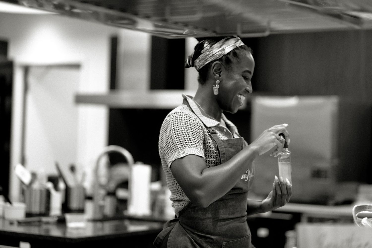 Smiling woman in apron laughs while working in a kitchen.