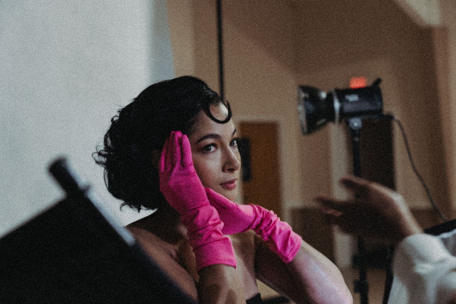 Woman in pink gloves poses during a photo shoot with studio lighting in the background.