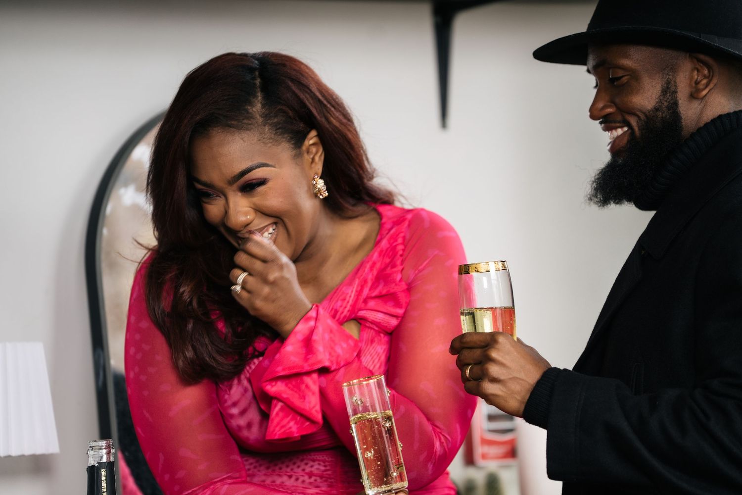 Woman in pink dress laughing joyfully while man holds champagne glass nearby.