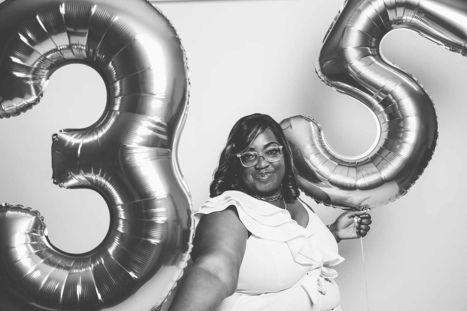 Black and white photo of woman holding number 35 balloons at birthday celebration.