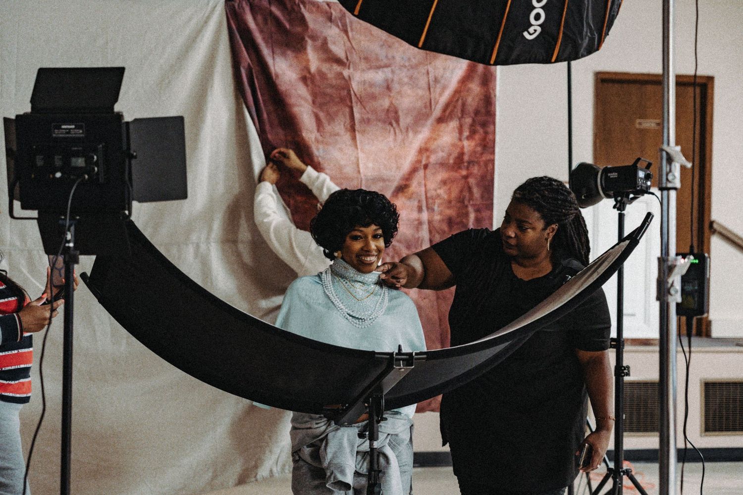 Behind the scenes of a photo shoot with a stylist adjusting a model's look in front of studio lights.