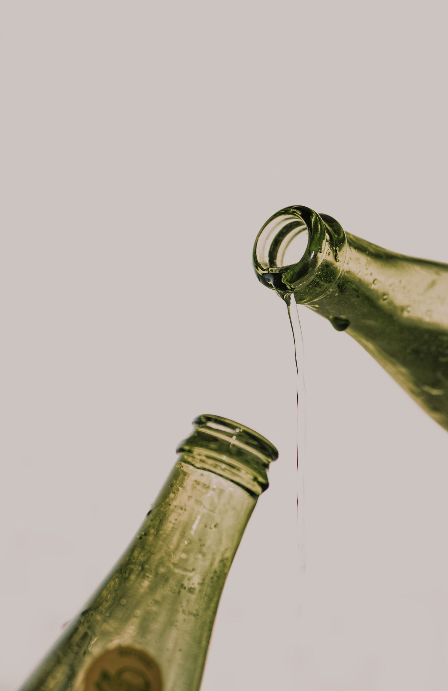 Two green glass Topo Chico bottles with water dripping from one into the other.