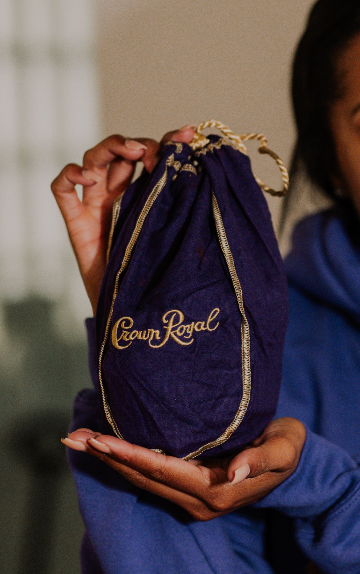 Hands holding a purple Crown Royal drawstring bag with gold embroidery.