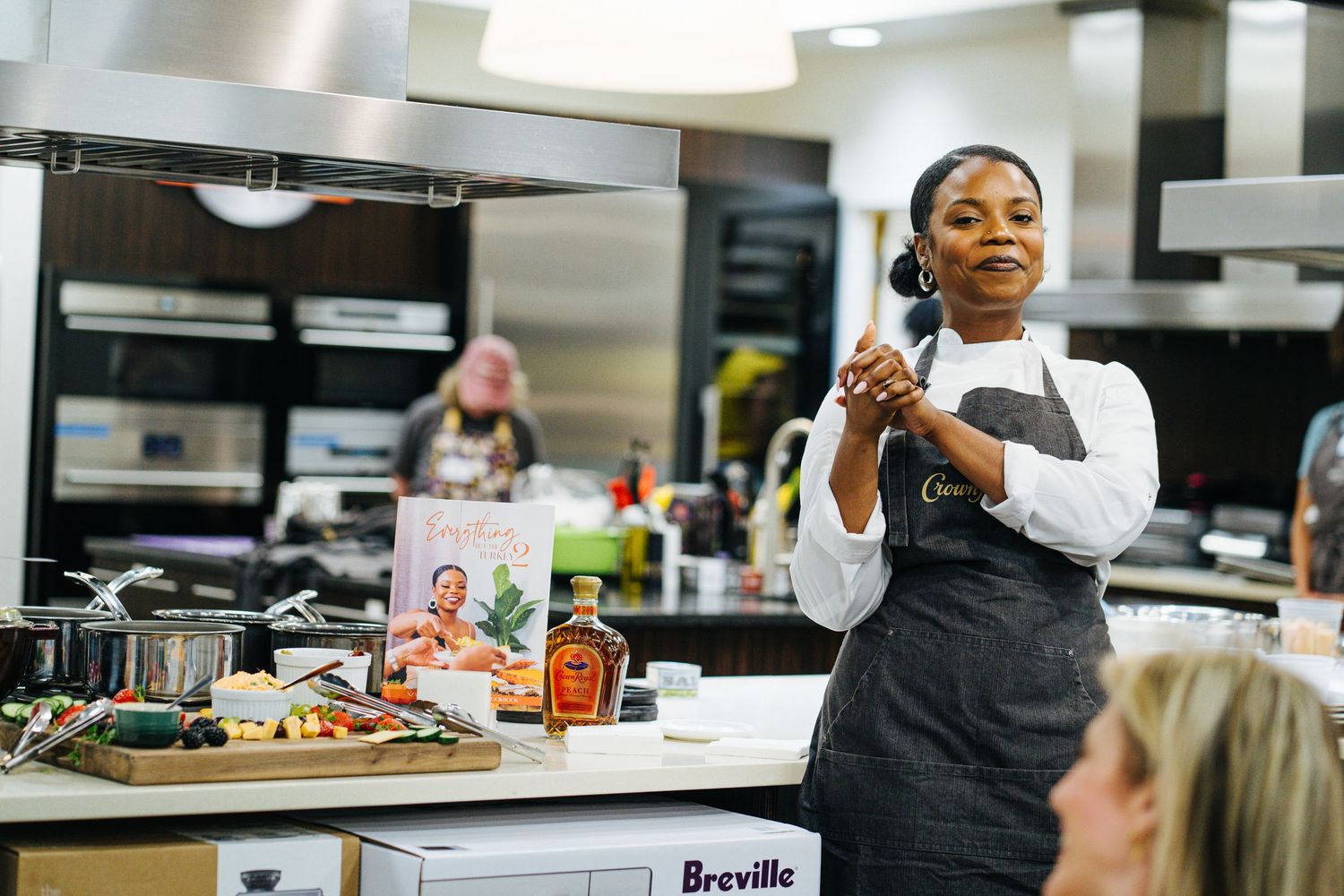 Chef in Crown Royal apron presents a cooking demonstration beside a Breville appliance.