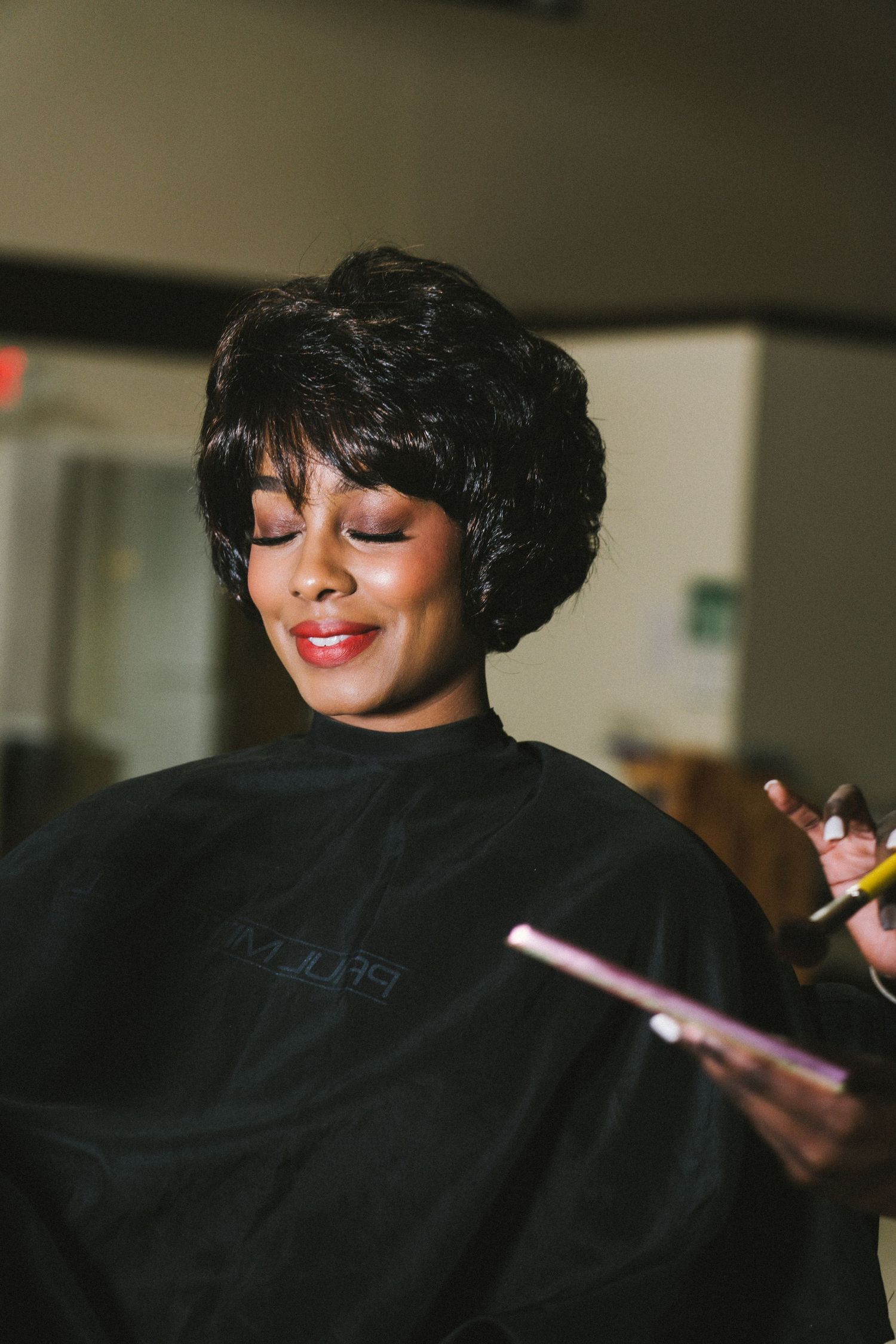 A woman with a styled bob haircut smiles during a hair salon appointment.