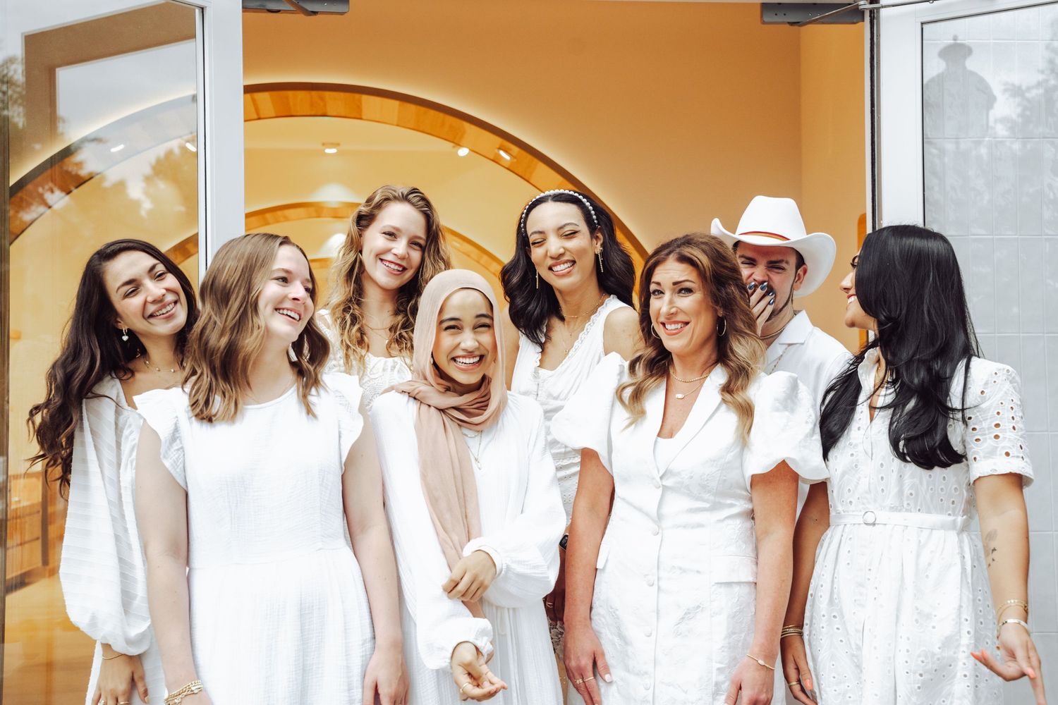 Group of diverse women in white outfits smiling together outside a Kendra Scott store.