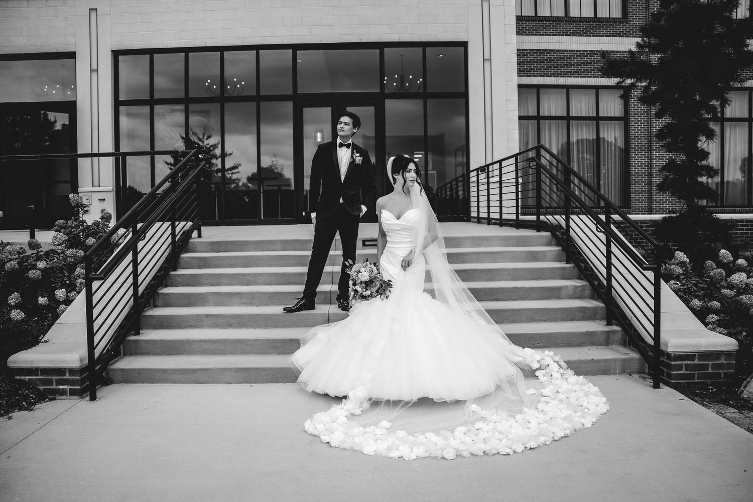 Black and white photo of a bride and groom posing on outdoor steps of an elegant venue.