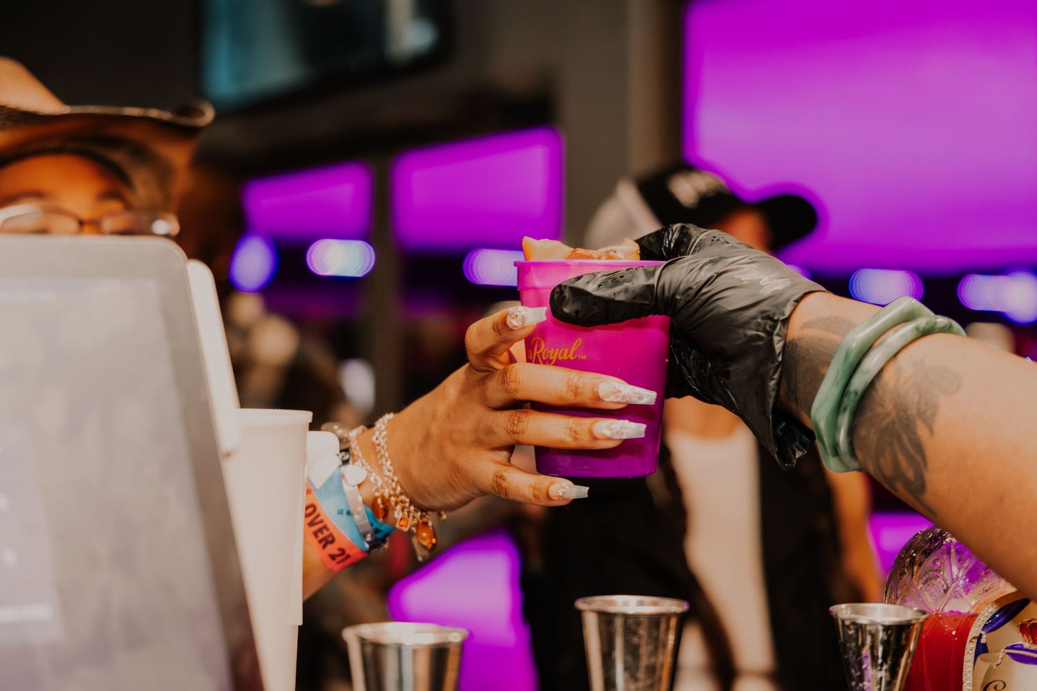 Bartender hands a pink cup to a customer at a colorful bar.
