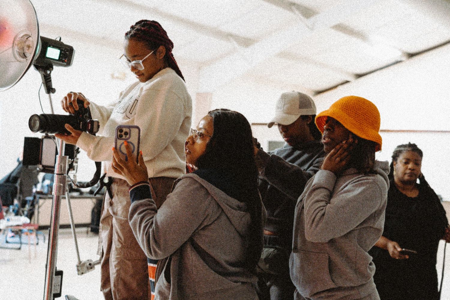 A group of women observe a photo shoot, with one standing on a ladder holding a camera.